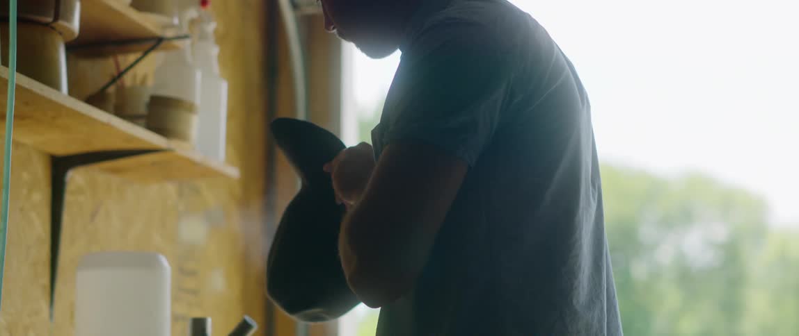 A man with a cowboy hat steaming a hat in a garage