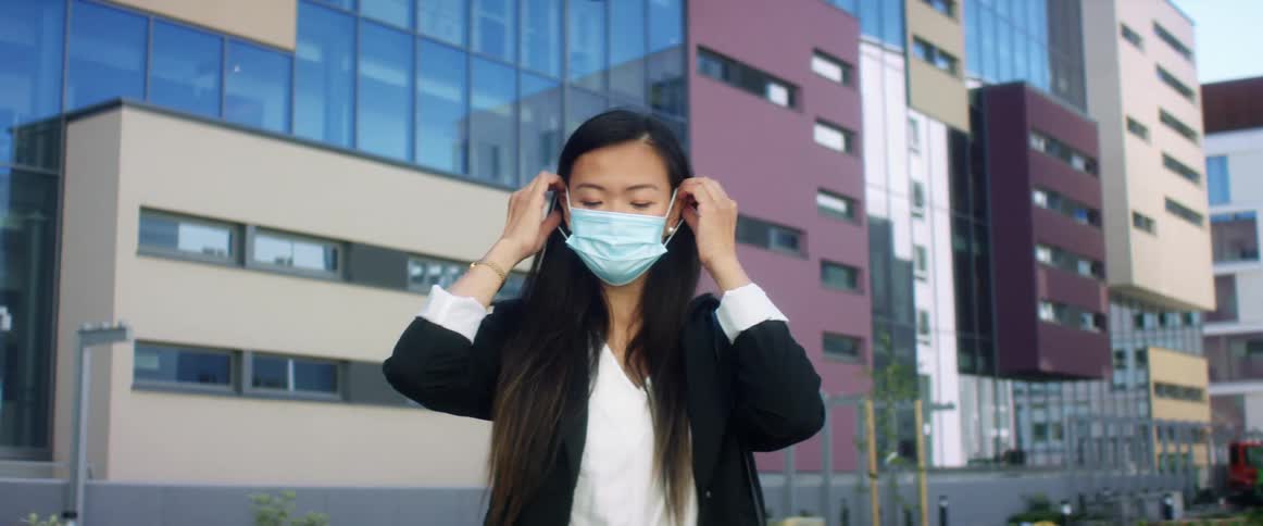 A woman puts on a face mask in a downtown city