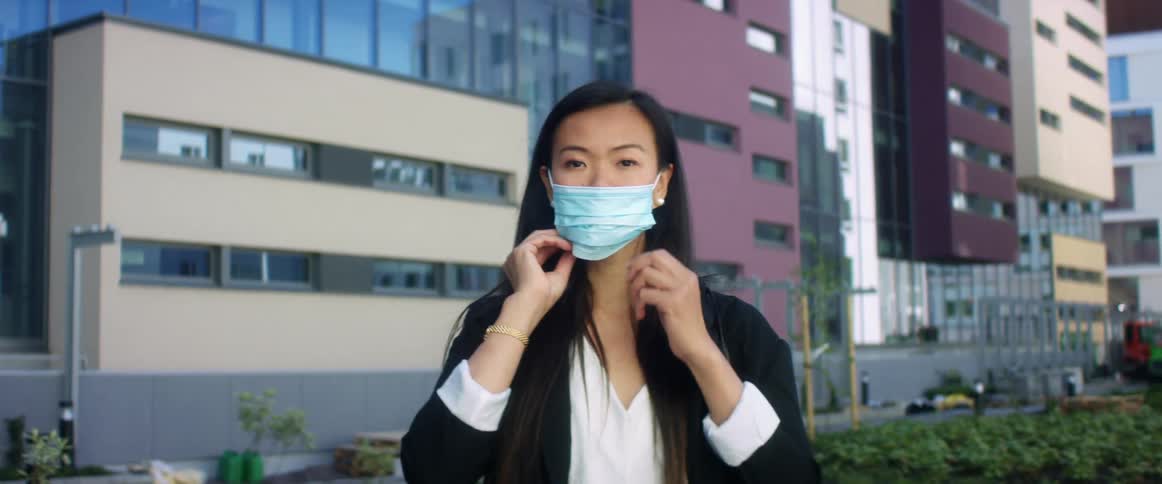 A woman is putting on a face mask in a downtown city
