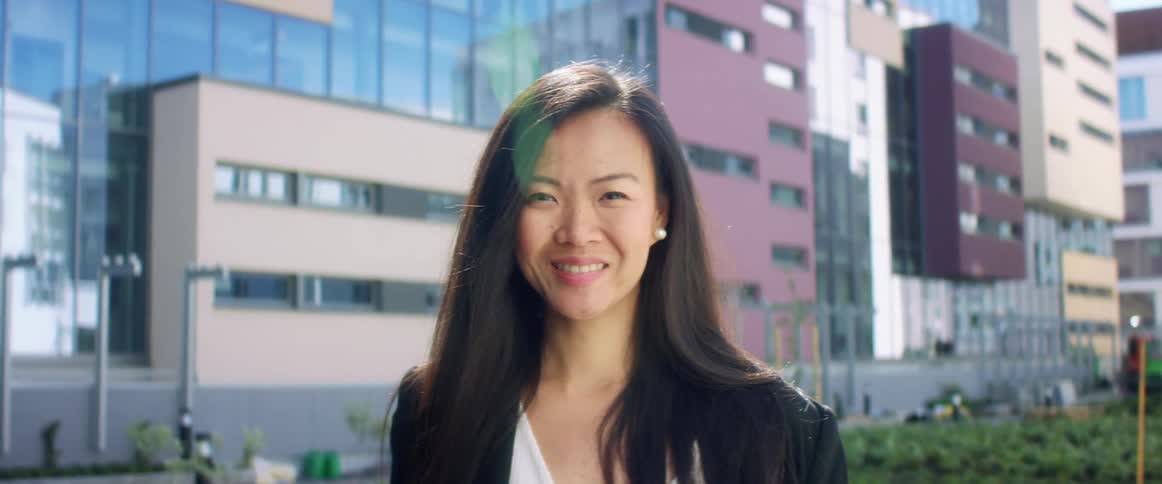 Asian woman with a blazer a shirt and long hair looks at the camera smilingly