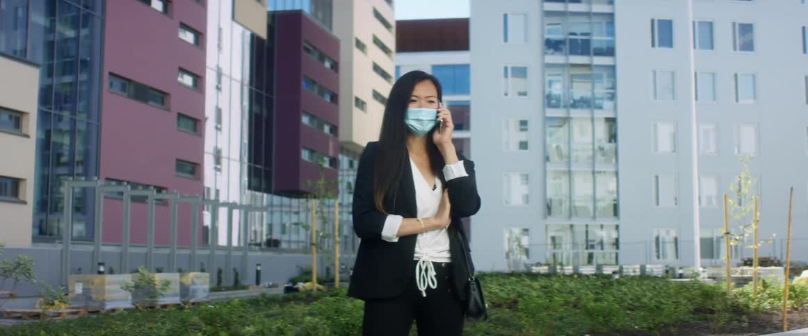 A woman stands outside apartment buildings and talks on her cell phone