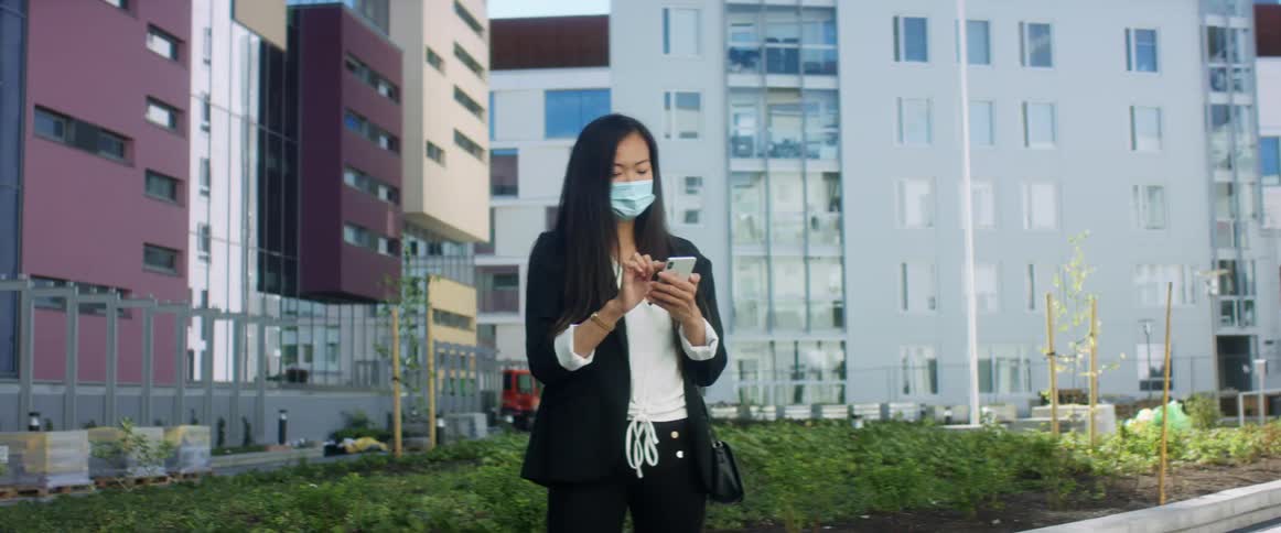 Woman wearing a face mask outside a building in the city makes a call on her smart phone