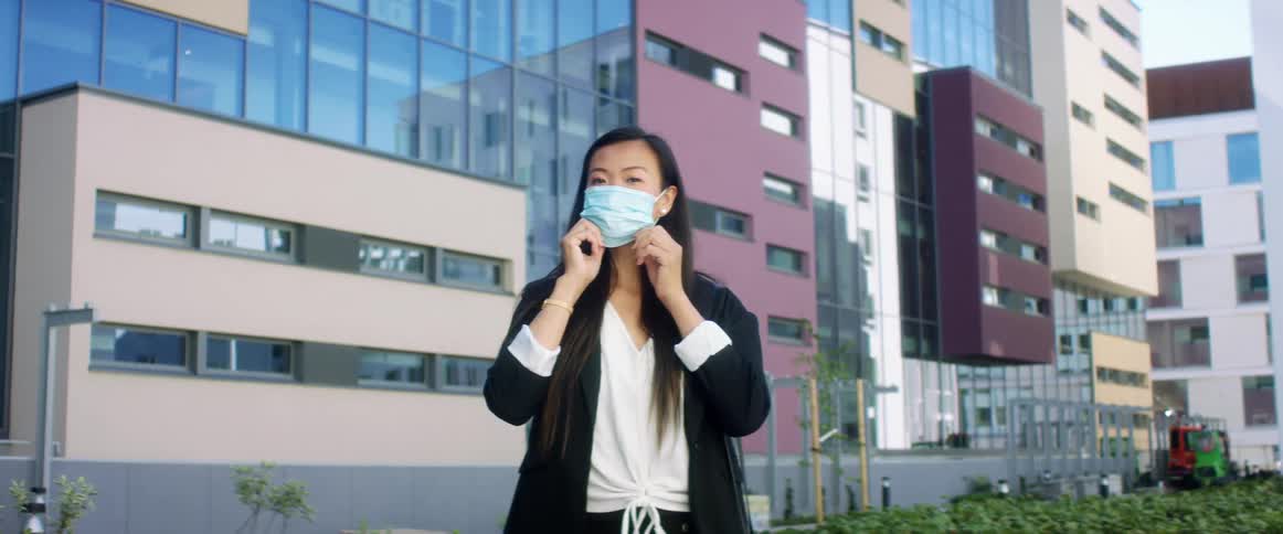 Young woman puts a face mask on while standing next to a building in the city