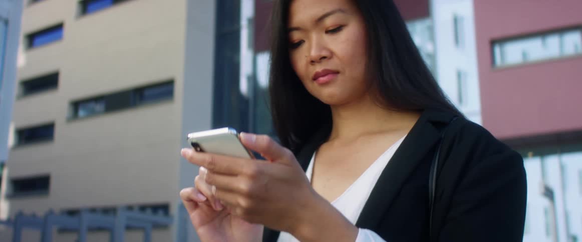A woman uses her smartphone while standing near tall buildings downtown
