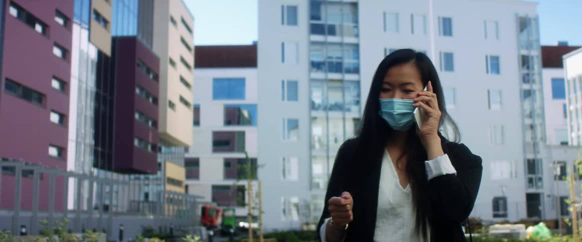 Woman wearing a face mask talks on her smart phone on the street of a city
