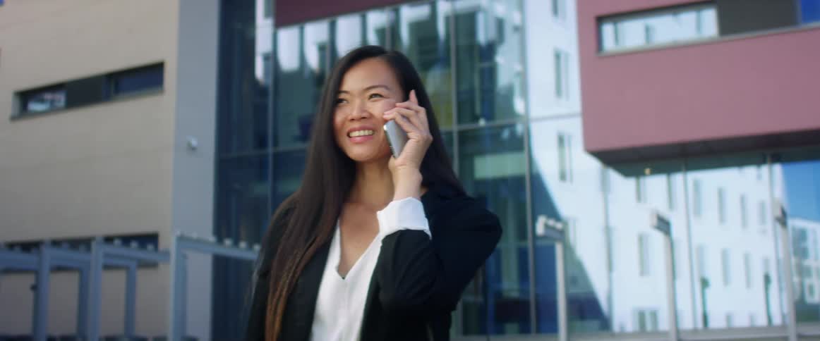 A woman standing and talking on a smart phone with a building in the background