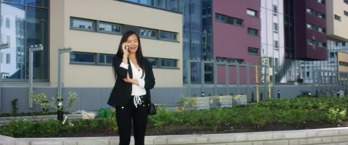 Woman stands near raised flowerbed talking on mobile phone with buildings in backdrop