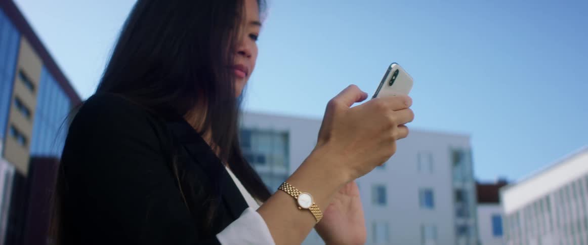 A woman is standing in a downtown city and texting on a cellphone