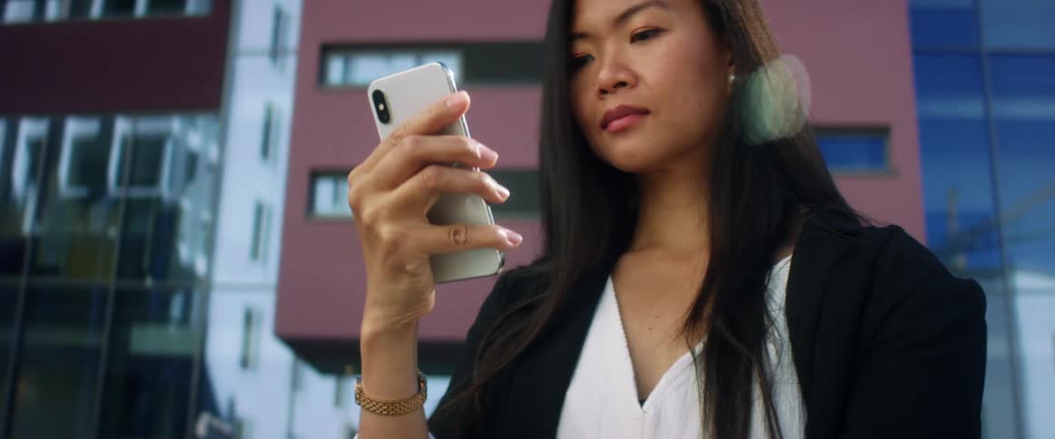Woman wearing business attire stand near buildings viewing mobile phone screen