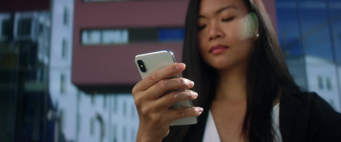 Asian woman with long hair uses iphone xs in the city street