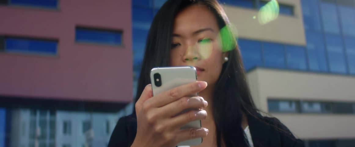 A young woman standing outside of an office building uses her phone