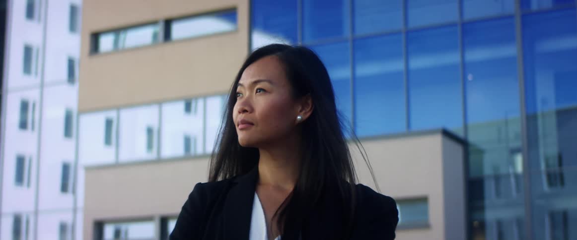 A young woman stands in a downtown area and looks up at office buildings