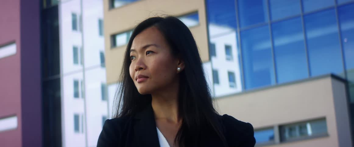 An asian woman stands outdoors and looks off into the distance as she poses for the camera