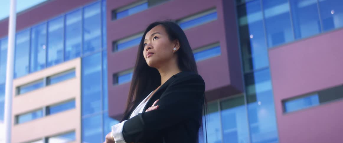 Woman wearing blazer stands outside buildings with arms crossed