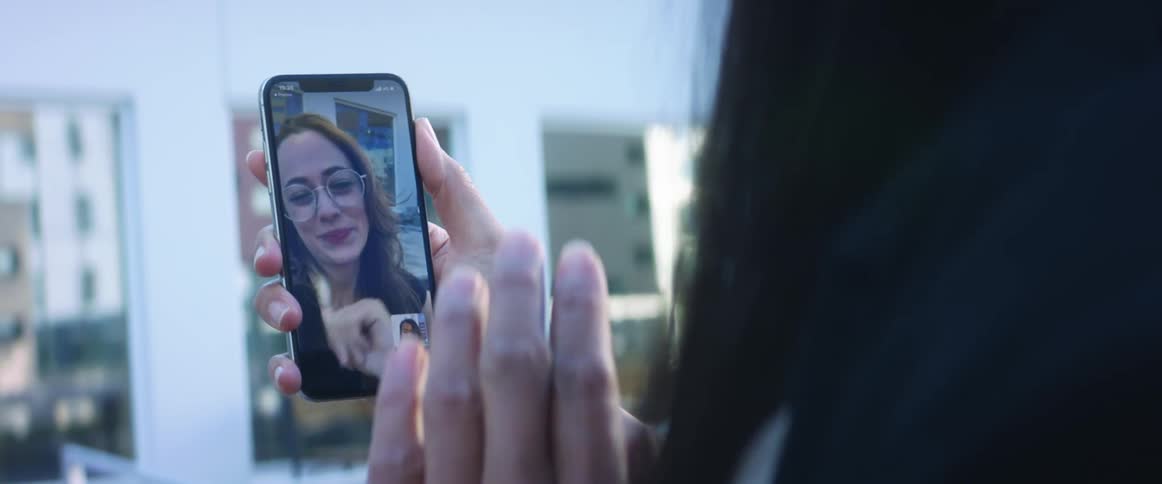 A woman holds up a cell phone and waves to the woman she is video chatting with