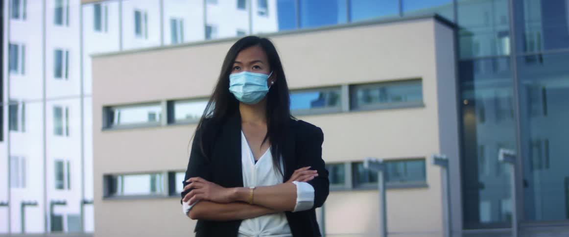 A woman is standing in an urban city while wearing a face mask