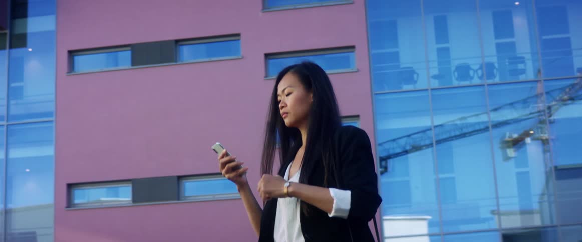 Woman uses smartphone while walking near a building in the street
