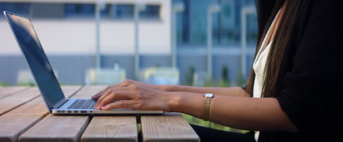 Woman with a white shirt and a black jacket sits at a table and opens a laptop with hand