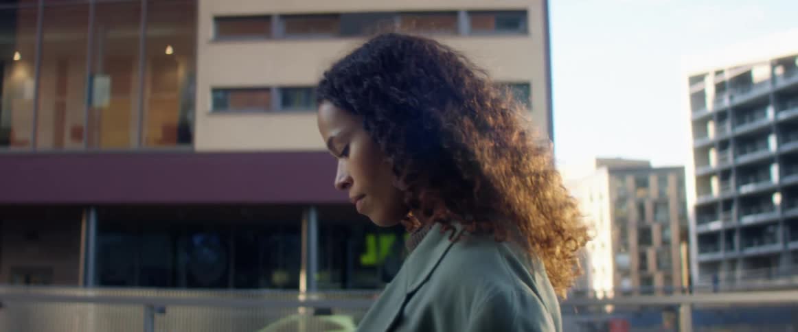 Side view of a black woman with curly hair and a blue overcoat walking down the street