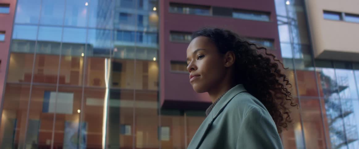 Black woman with curly hair and a blue topcoat walks down the city street