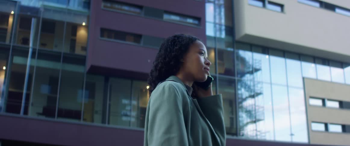 A woman standing and talking on a smartphone with a building in the background