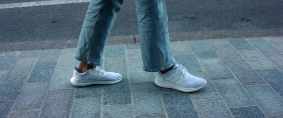 Person in jeans and white sneakers walks along brick sidewalk near street encountering covered manhole