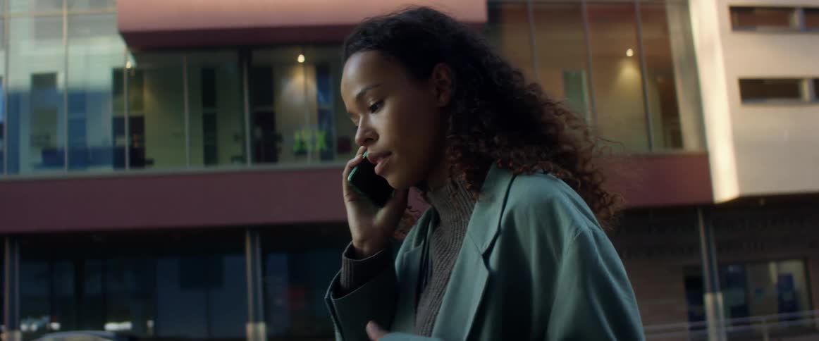 A young black woman talks on a smartphone while standing outdoors in a city during the day