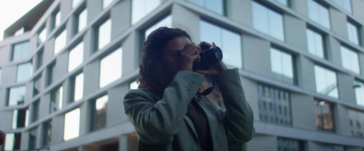 Black woman with curly hair and a blue top coat takes photographs and checks them in the street