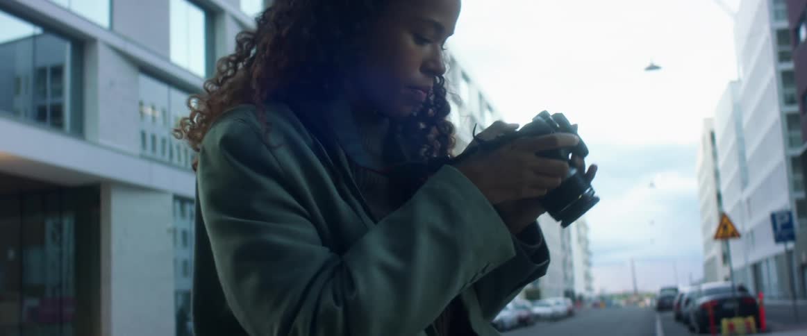 A woman holds a camera to her face standing in the road of a city