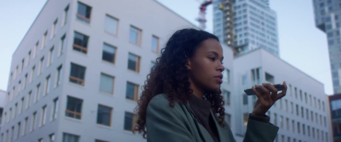 A woman stands outside of large city buildings talking on her cell phone