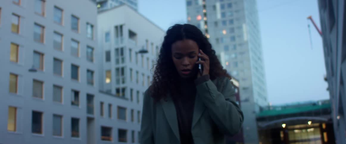 Black woman talks on a cell phone as she paces back and forth near the city buildings