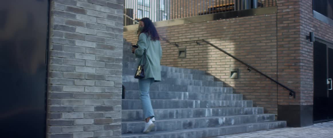 Black woman with curly hair and jeans turns around and goes up the stairs in the street