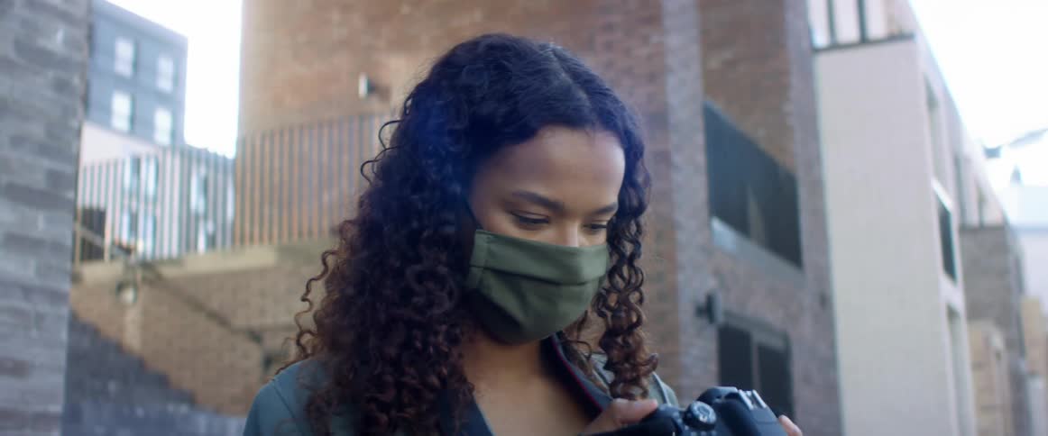 A woman stands outside a city building looking at the screen of her camera