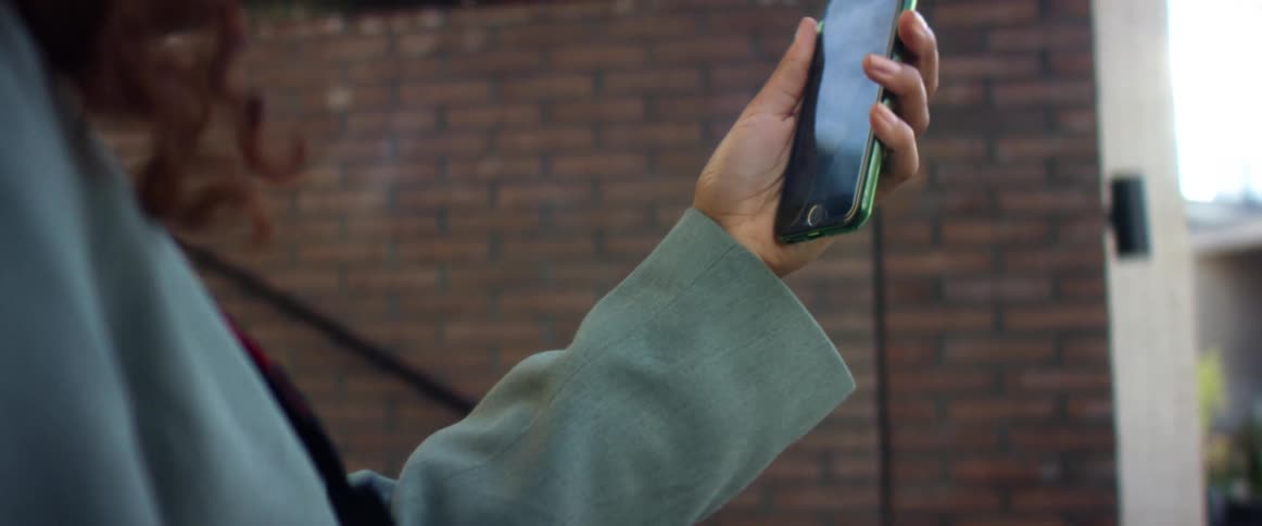 Woman holds a smartphone on her hand while standing next to a building