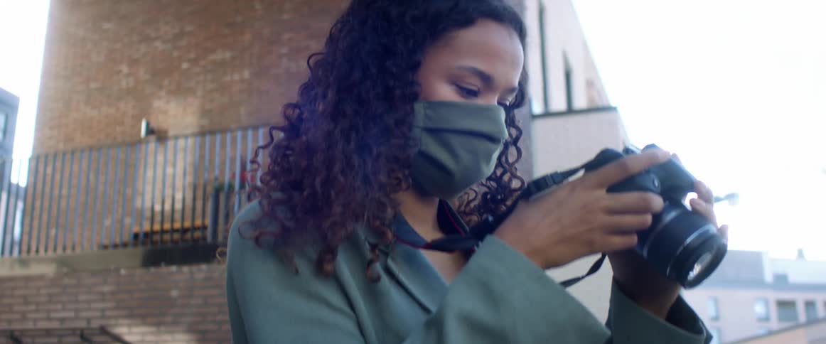 Black woman with curly hair and a blue top coat takes photographs and checks them in in a street