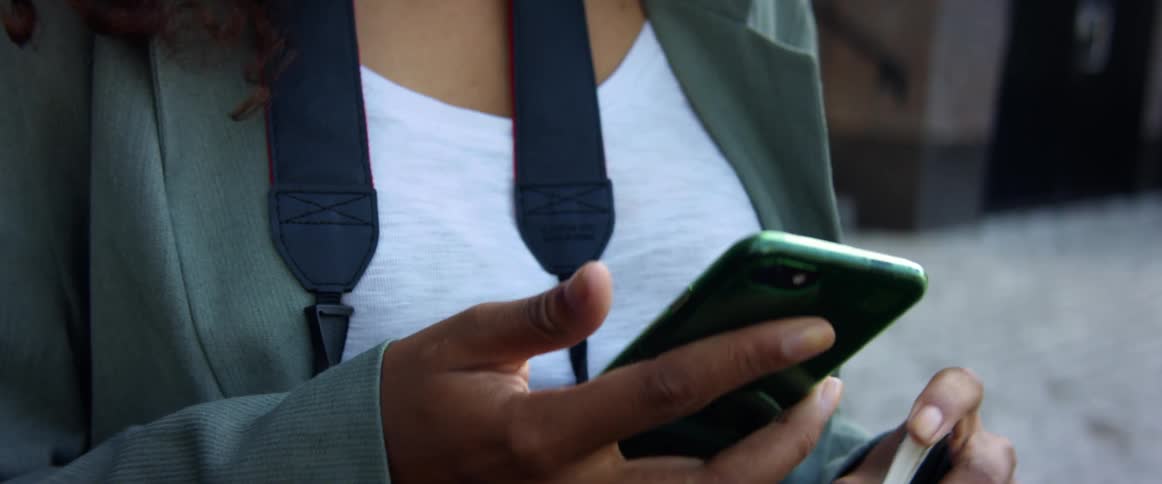 A woman standing outdoors types on a smartphone with her thumb