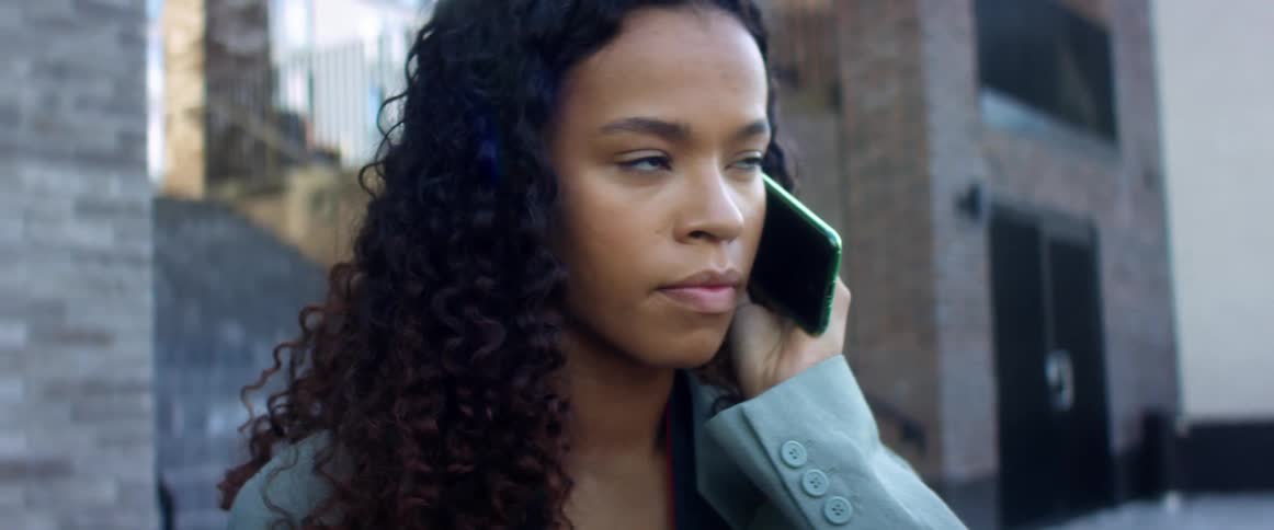 Black woman with curly hair and a blue coat makes a phone call in the street