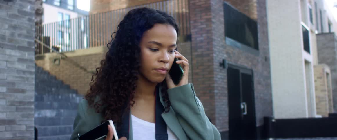 A woman is standing outside of a building and talking on a cellphone