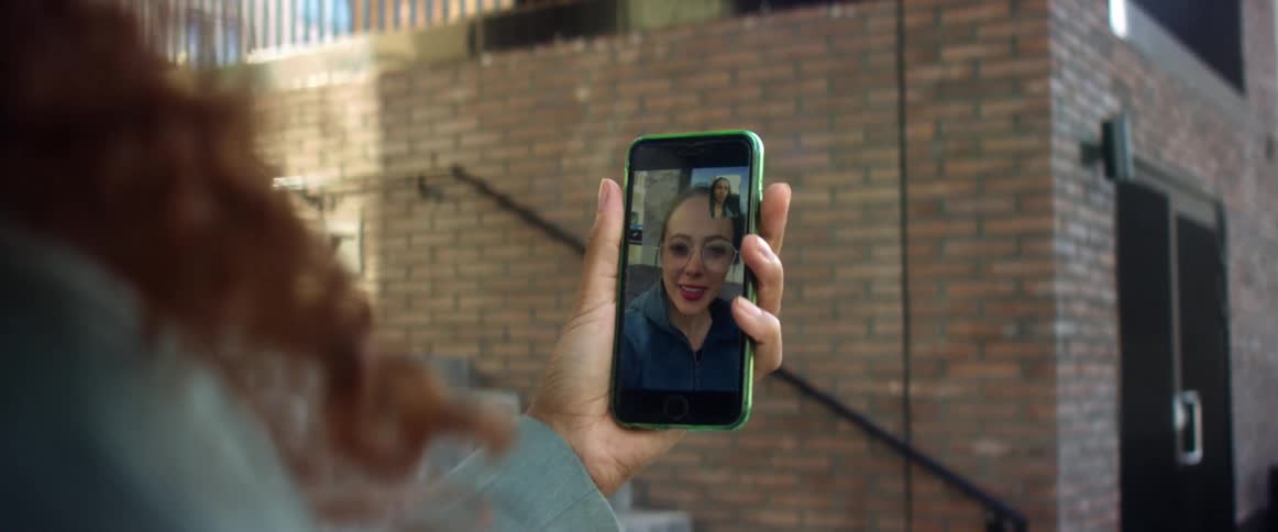 A woman holding a smart phone in her hand and video chatting with a building in the background