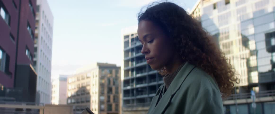 A young woman carrying a tablet in a case walks across a bridge in a metropolis during the day