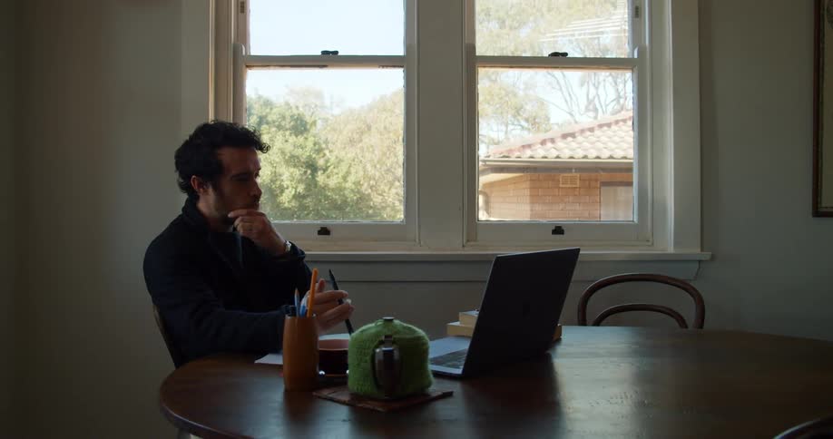 A man sits at a dining room table working at his laptop