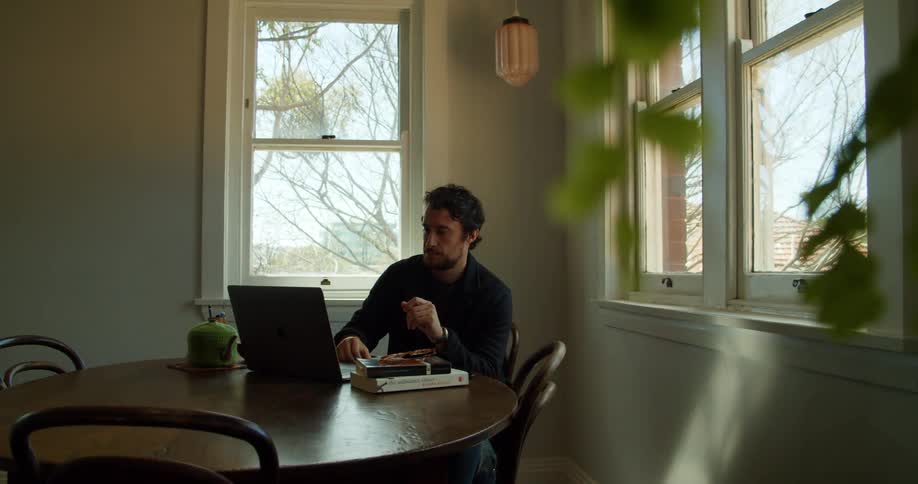 A man sitting at home video chats on his laptop and writes something down