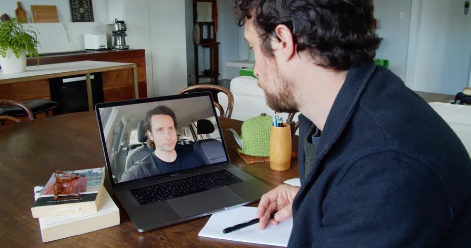 Two man talk to each other via video chat while one sits in front of his laptop
