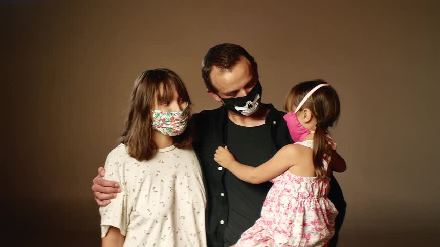 A man holds his daughter and he and his wife pose with face masks on