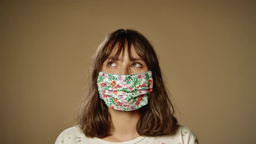 Woman with brown wavy hair and a floral mask faces the camera without eye contact