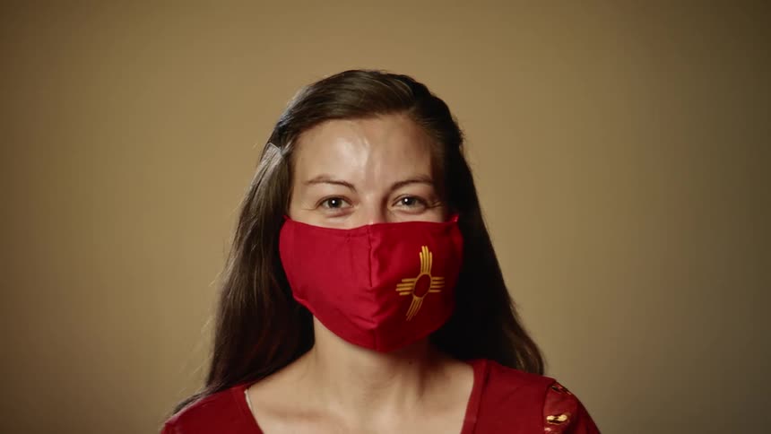 A woman with a gray streak in her hair poses in a red face mask and red shirt