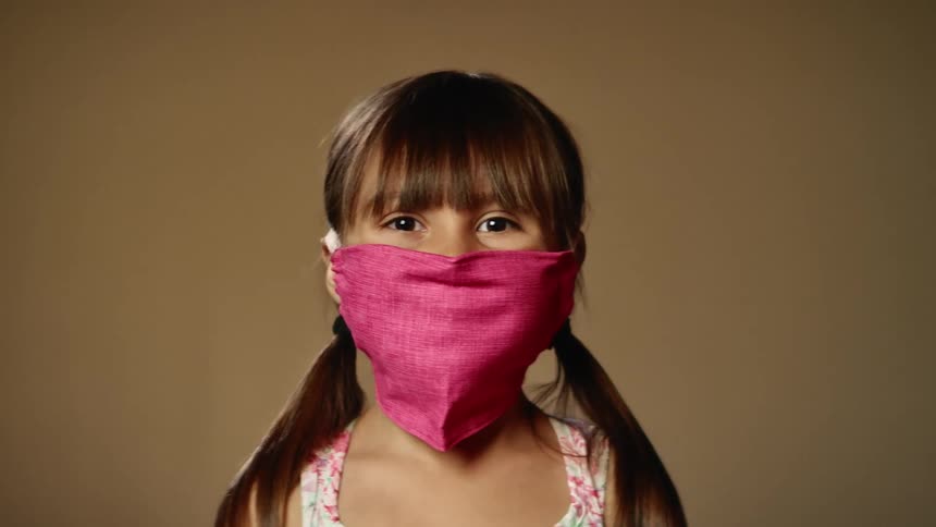 A young girl wearing a mask stands in a studio for a photo