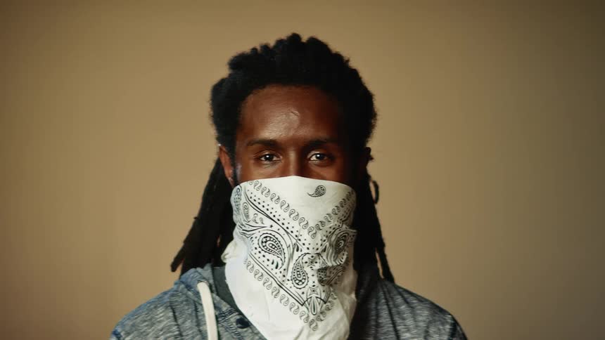 A man wearing a bandana as a mask is staring toward the camera