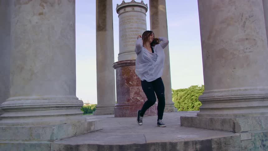 Young woman dancing on monument with large pillars