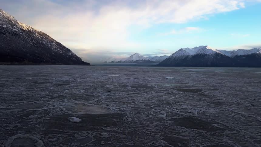 A frozen tundra is surrounded by snow capped mountains